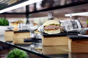 Ein Sandwich, das in eine Zeitung eingewickelt ist, steht auf einer Glasplatte.