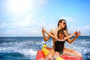 Eine Frau und ein Kind auf einem Banana Boat im Ozean, beide lächeln und genießen den Tag.