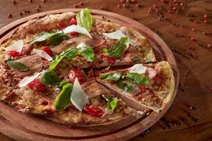 Eine Pizza mit Schinken und Basilikum auf einer Holzplatte.