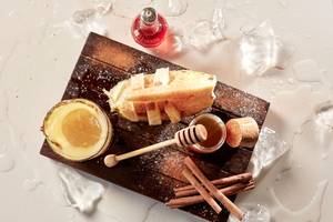 Avra Imperial Essenz Cocktail auf einem Holzbrett mit Eiswürfeln, Zimtstangen und Honig.