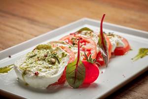 Ein Gericht mit Mozzarella und Tomaten auf einem weißen Teller, dekoriert mit grünen Pesto und Basilikumblättern.
