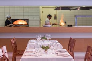 Restaurantszene im Avra Imperial Hotel mit Koch, der Flammen erzeugt, und Kellnerin hinter Ofen