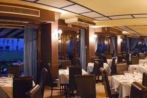 Innenansicht des Restaurants im Hersonissos Palace Hotel mit gedeckten Tischen und Stühlen, blauen Vorhängen und Lampen.