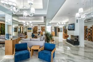 Lobby des Odyssia Beach Hotels mit modernen Möbeln, hellen Wänden und hängenden Kronleuchtern.