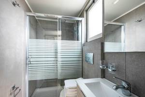 Badezimmer des Odyssia Beach Hotels mit einer Glasdusche, einem Waschbecken und einem Spiegel.
