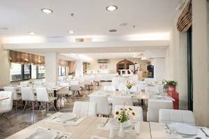 Innenbereich des Speisesaals im Odyssia Beach Hotel mit weißen Möbeln und Tischdekoration.