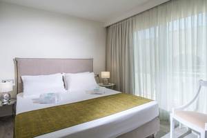Schlafzimmer im Odyssia Beach Hotel mit Bett, Kissen, Lampen und Fenstern.