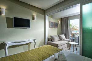 Innenansicht eines Zimmers im Odyssia Beach Hotel mit Fernseher, Couch und Tisch.