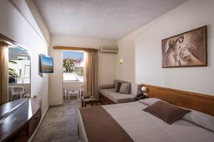 Innenansicht eines Hotelzimmers im Odyssia Beach Hotel mit Doppelbett, Sofa und Balkon.