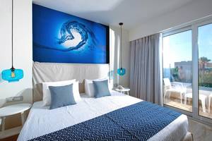 Schlafzimmer im Odyssia Beach Hotel mit blauer Wand, Doppelbett und großem Fenster.