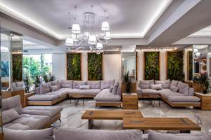 Hotel Odyssia Beach Lobby-Loungebereich mit grauen Sofas, Holztischen und Pflanzen
