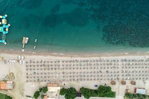 Luftaufnahme des Mitsis Norida Beach Hotels mit Strand, Wasserrutsche und vielen Liegestühlen.