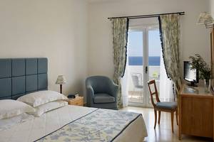 Schlafzimmer im Mitsis Norida Beach Hotel mit Meerblick, Bett, Sessel und Schreibtisch.