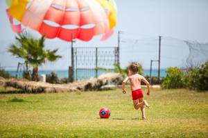 Ein junger Junge spielt mit einem Fußball am Strand, während ein Parasailing-Ballon im Hintergrund schwebt.