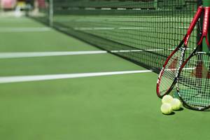 Tennisschläger und Bälle auf einem Tennisplatz neben einem Netz.