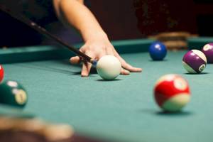 Eine Hand hält einen Poolstock und zielt auf eine weiße Kugel auf einem Pooltisch mit verschiedenen farbigen Kugeln.
