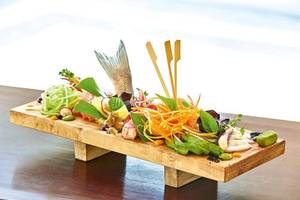 Ein Fischgericht auf einer Holzplatte mit verschiedenen Gemüsesorten im Grecotel La Riviera & Aqua Park Hotel.
