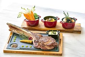 Ein Steak und Gemüse auf einer Holzunterlage mit Beilagen in Töpfen.