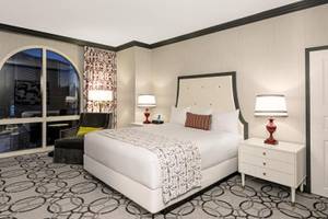 Hotelzimmer im Paris Las Vegas mit großem Bett, zwei Nachttischen und einem Sessel
