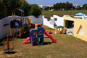 Kinderspielplatz im Freien beim Smy Kos Beach & Splash Hotel mit bunten Spielgeräten und einer Rasenfläche.
