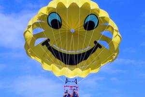 Zwei Leute im Parasailing mit gelber Parasegel mit Smiley-Gesicht.