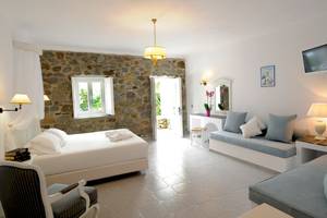 Kamari Hotel Schlafzimmer mit Doppelbett und Sofa, Steinwand, weißer Bettwäsche und Deko