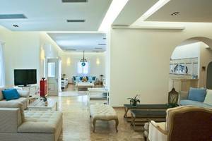 Wohnbereich des Kamari Hotels mit modernen Möbeln, Fernseher, Sofas, Couchtischen und Pflanzen.