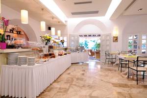 Frühstücksbuffet im Kamari Hotel mit vielen Speisen und Tisch mit Stühlen.