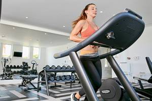 Eine Frau im Fitnessstudio läuft auf einem schwarzen Laufband.