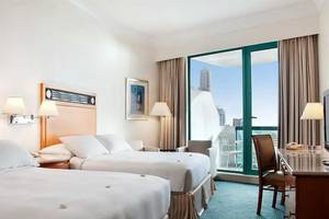 Hotelzimmer im Hilton Dubai Jumeirah Resort mit zwei Betten, Schreibtisch und Aussicht auf die Stadt.