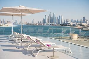 Terrasse des W Dubai - The Palm Hotels mit weißen Sonnenliegen und großen Sonnenschirmen.