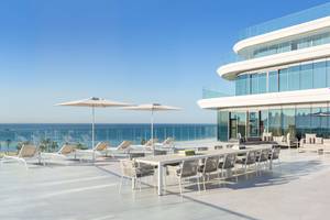 Außenterrasse des W Dubai - The Palm mit Blick auf das Meer, Lounge-Sesseln und Sonnenschirmen.