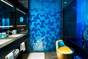 Badezimmer im W Dubai - The Palm Hotel mit blauer geometrischer Wandfliesen und gelbem Stuhl.