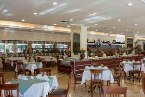 Speisesaal des Miramare Queen Hotels mit vielen Tischen und Stühlen, einer großen Essenstheke und dekorativen Elementen.