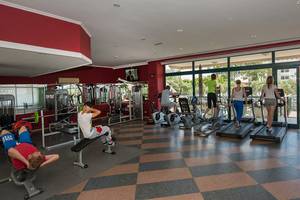 Fitnessstudio im Miramare Queen Hotel mit verschiedenen Trainingsgeräten und Personen, die trainieren.