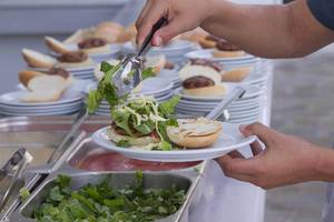 Eine Person serviert einen Burger auf einem weißen Teller in einem Buffet.