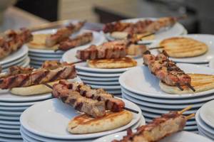Mehrere gestapelte weiße Teller mit marinierten Fleischspießen und Pita-Brot