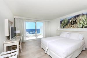 Ein modernes Hotelzimmer mit zwei Betten, Blick auf das Meer und eine Terrasse.