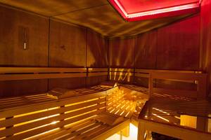 Innenansicht der Sauna im Lopesan Villa del Conde Resort & Thalasso mit Holzbänken und roter Beleuchtung.
