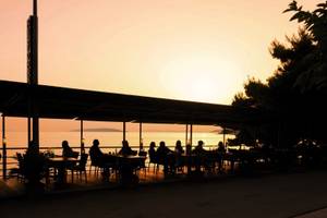 Gaste sitzen auf der Terrasse des Saudade Hotels bei Sonnenuntergang mit Blick auf das Meer.