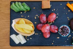 Verschiedene Obstsorten und Snacks auf einem schwarzen Tablett auf einem Holztisch.