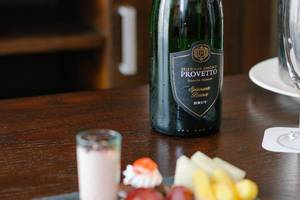 Eine Flasche Provento Spumante Bianco Brut neben einem Glas und kleinen Happen auf einem Tisch.