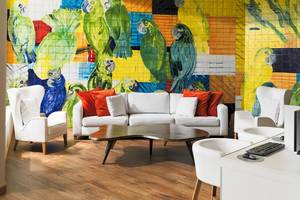 Wohnzimmer mit weißem Sofa, rote Kissen und bunter Wandmalerei von Papageien.