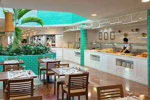 Restaurant im H10 Playa Esmeralda Hotel mit grünen Wänden und blauen Fliesen, servierenden Kellnern und gedeckten Tischen.