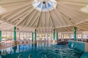 Innenbereich des Poolbereichs im H10 Playa Esmeralda Hotel mit Glasdach und grünen Säulen