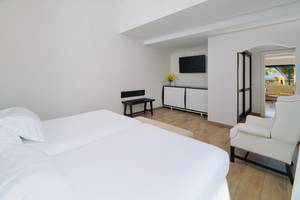 Schlafzimmer im H10 Playa Esmeralda Hotel mit weißen Möbeln, Holzboden und Blick auf den Balkon.