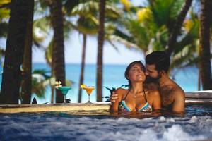 Paar im Pool beim Catalonia Royal Tulum Hotel mit Blick auf den Ozean und Palmen