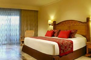 Bett im Hotelzimmer des Catalonia Royal Tulum mit rotem Kopfteil und weißen Laken.