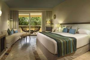Ein modernes Hotelzimmer im Catalonia Royal Tulum mit einem großen Bett, einem Sofa und einem Balkon mit Möbeln.
