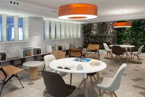 Loungebereich im Hotel Tigotan Lovers & Friends mit weißen Möbeln, grüner Wand und mehreren Tischen.